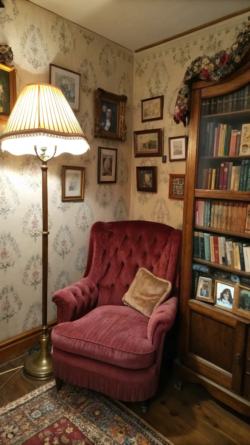 Cozy reading corner at dusk with burgundy velvet armchair, wooden bookshelf full of classics, family photos, brass floor lamp, and handmade afghan.