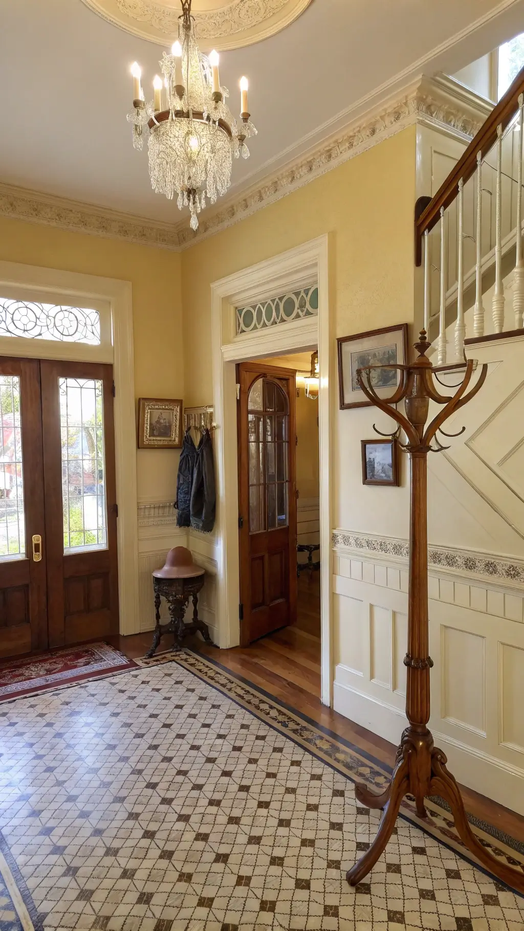 1920s styled entryway featuring wainscoting, hardwood floors, a crystal chandelier, a Victorian hall tree, gilded mirror, copper umbrella stand, family photographs, and a collection of vintage scarves and hats.
