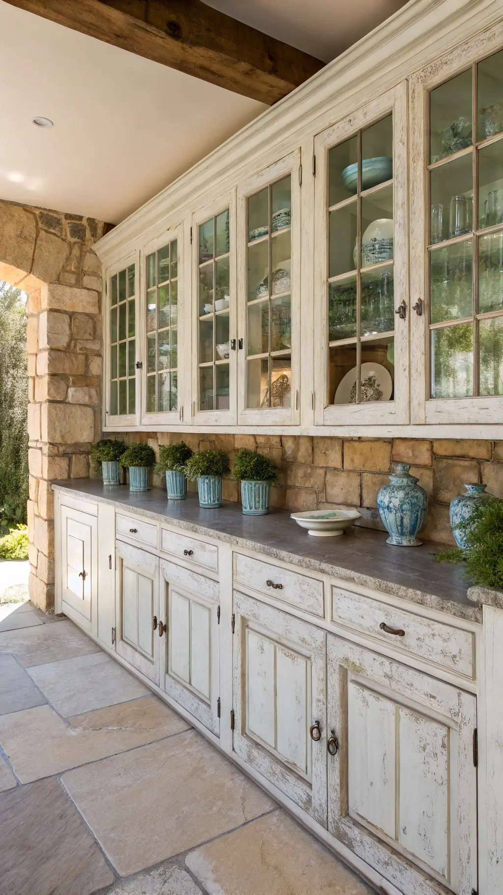 Sunny country kitchen with white distressed cabinets, natural pine lower units, and stone backsplash with climbing herbs, highlighted by light entering through French doors
